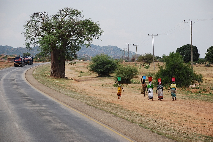 Tanklastwagen transportieren Petroleum auf der Strasse und Frauen Wasser auf ihren Köpfen