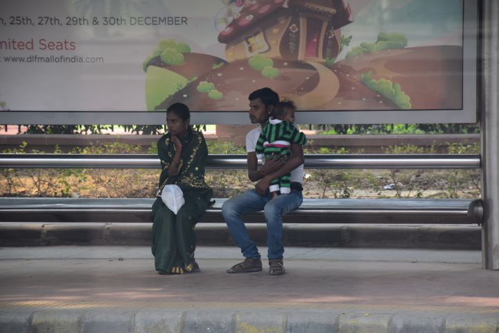 Junge Familie an einer Bushaltestelle in Neu-Delhi