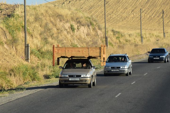 Auto transportiert ein grosses Bett quer auf dem Dach