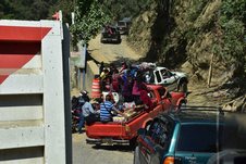 Pick-ups beladen mit Menschen und Waren fahren auf eine steile Bergstrasse